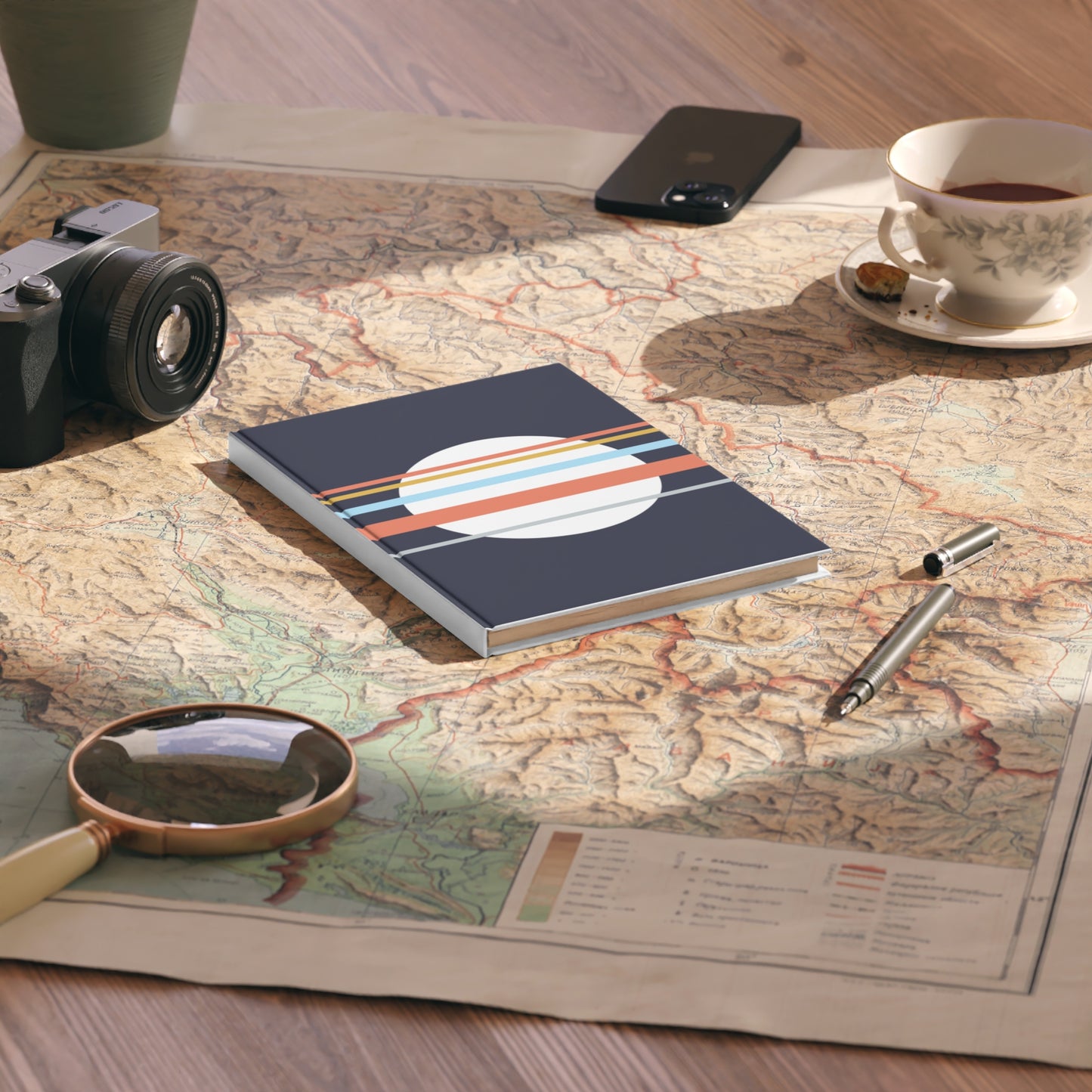 Notebook with a colorful design on a map with a camera, phone, cup, and pen.