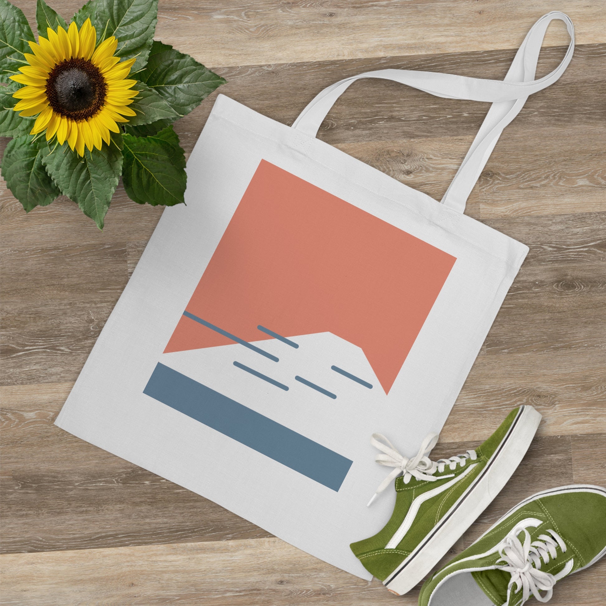 Tote bag with mountain design, green sneakers, and sunflower on wooden surface