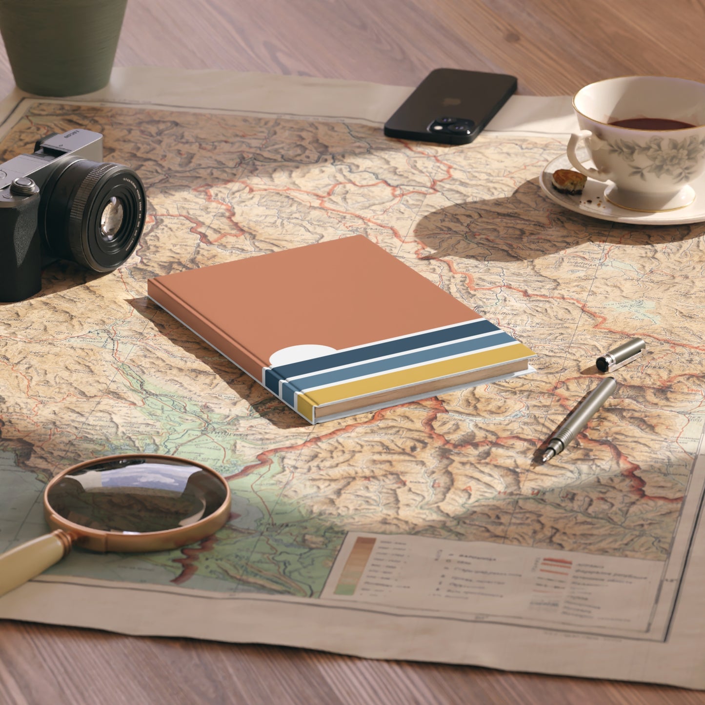 Notebook with striped cover on a map with camera, phone, cup, and pen nearby