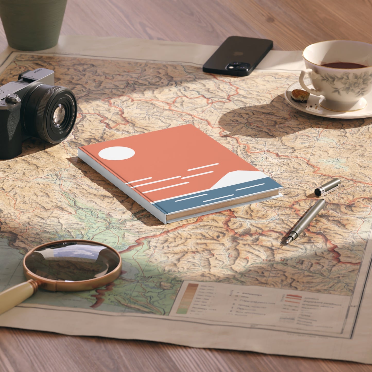 Notebook on a map with a camera, phone, and tea cup in the background