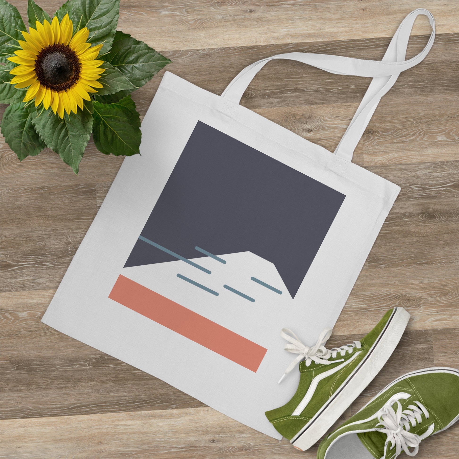 Tote bag with mountain design, sunflower, and green sneakers on a wooden surface