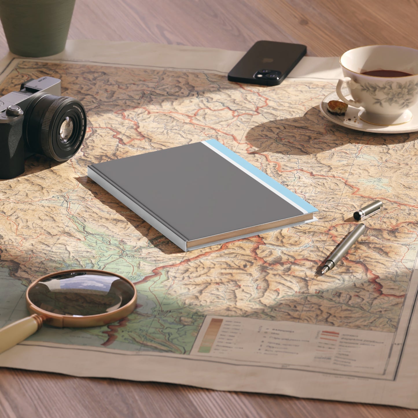 Notebook, camera, magnifying glass, and tea cup on a map