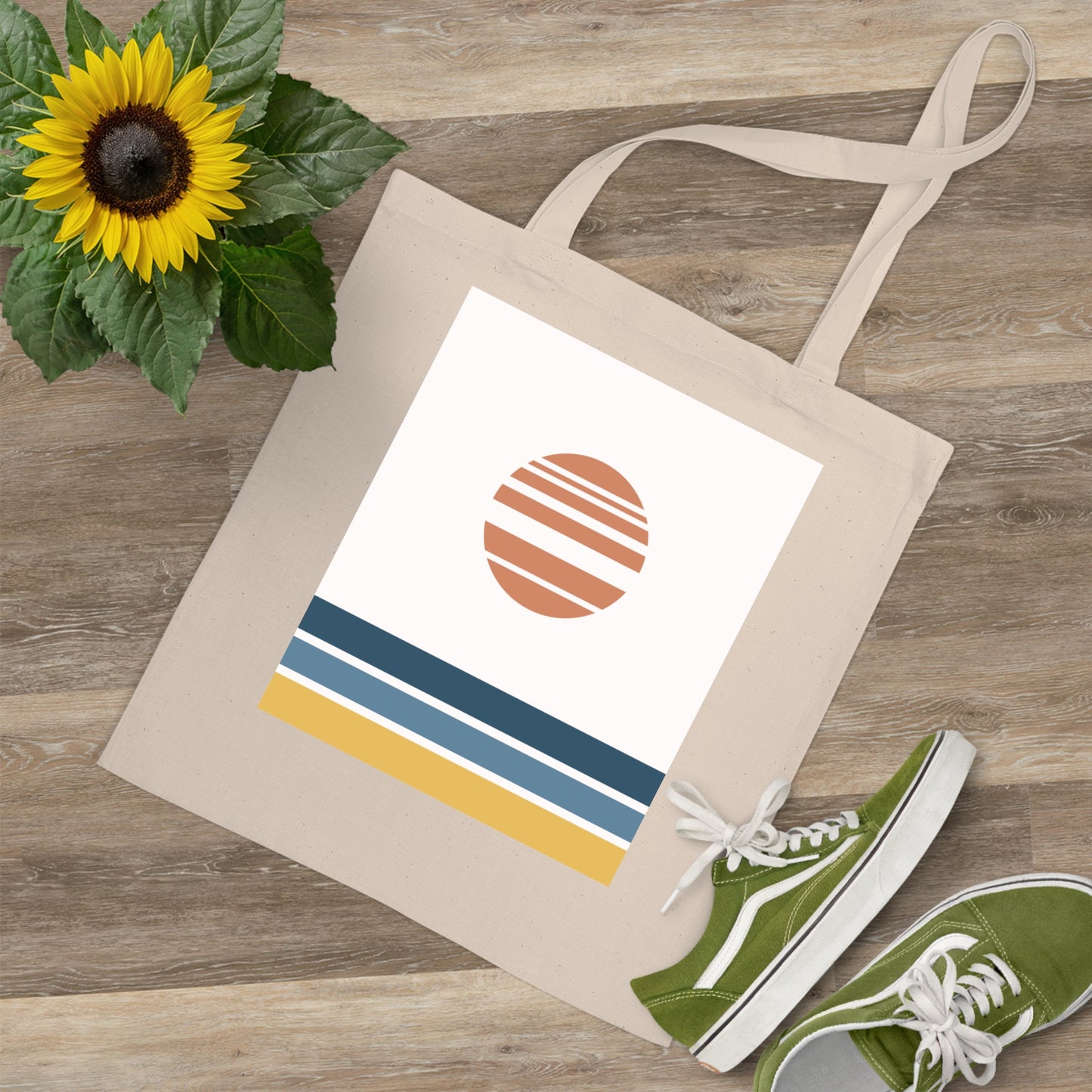 Beige tote bag with a colorful design, green sneakers, and a sunflower on a wooden surface.