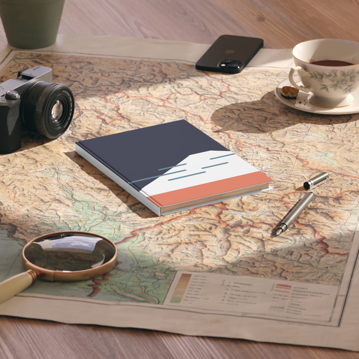 Notebook on a map with a camera, phone, cup of tea, and pen nearby