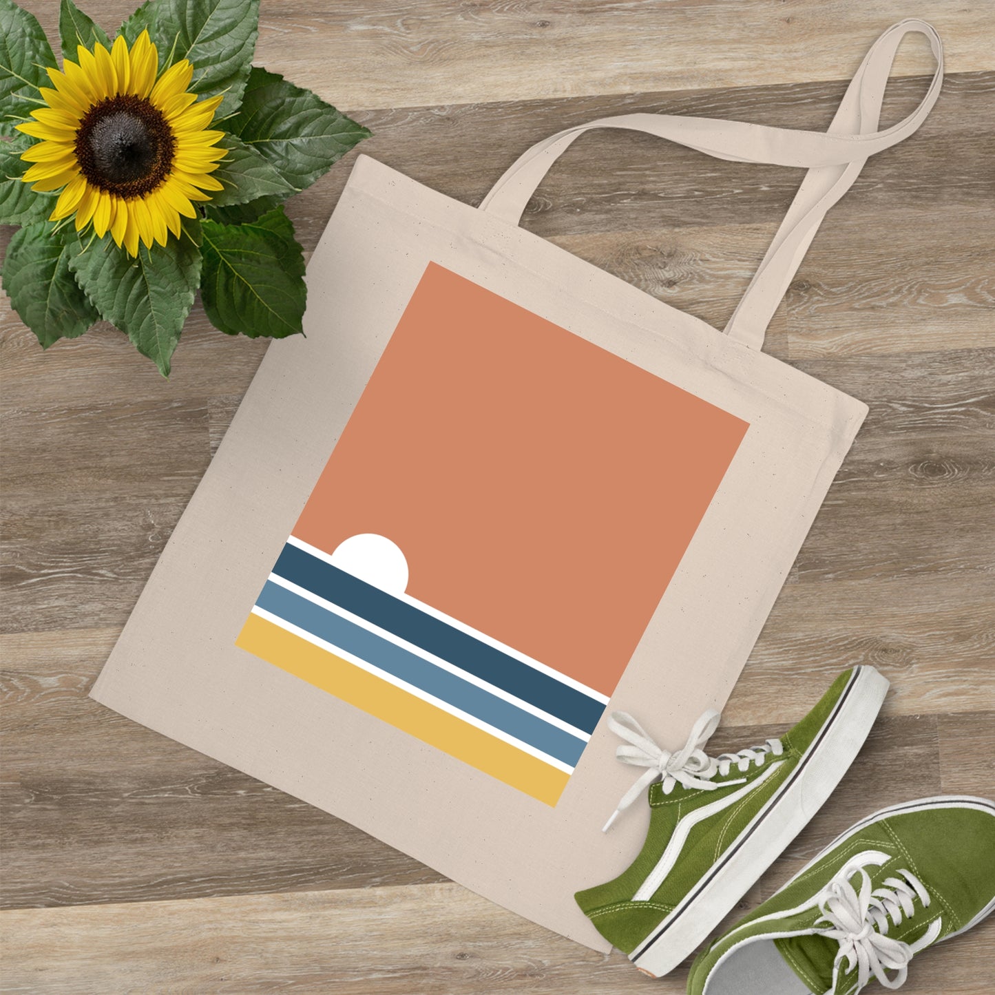 Tote bag with a colorful design on a wooden surface with green shoes and a sunflower.