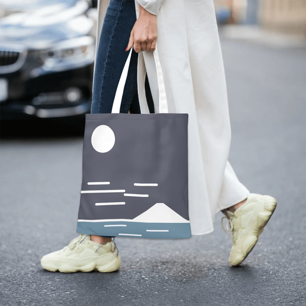 Person walking on a street holding a tote bag with a mountain design.