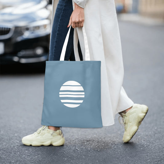 Person holding a blue tote bag with a white logo on a street.