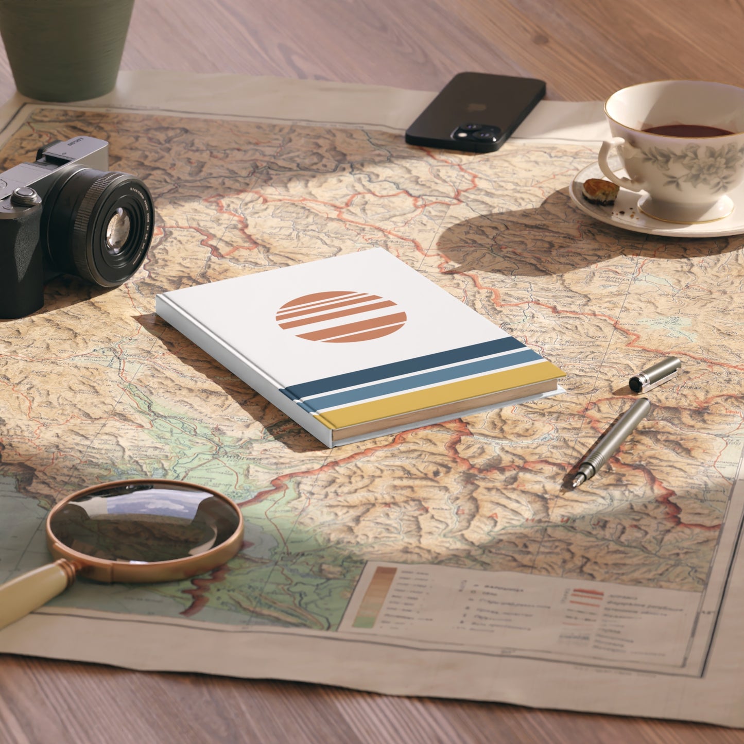 Notebook with a sun design on a map with a camera, phone, cup, and pen.