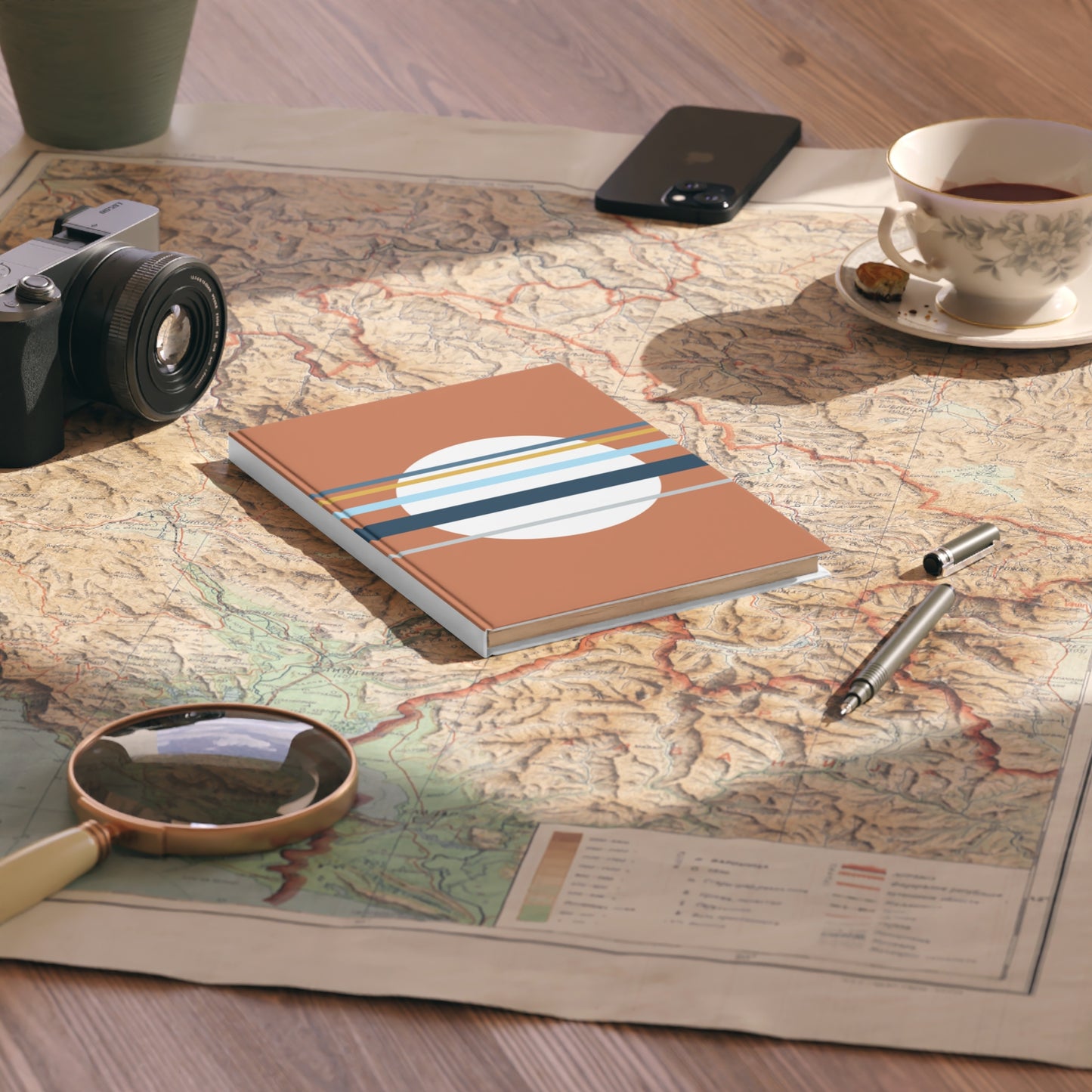 Notebook with travel-themed design on a map with camera, phone, cup, and pen.