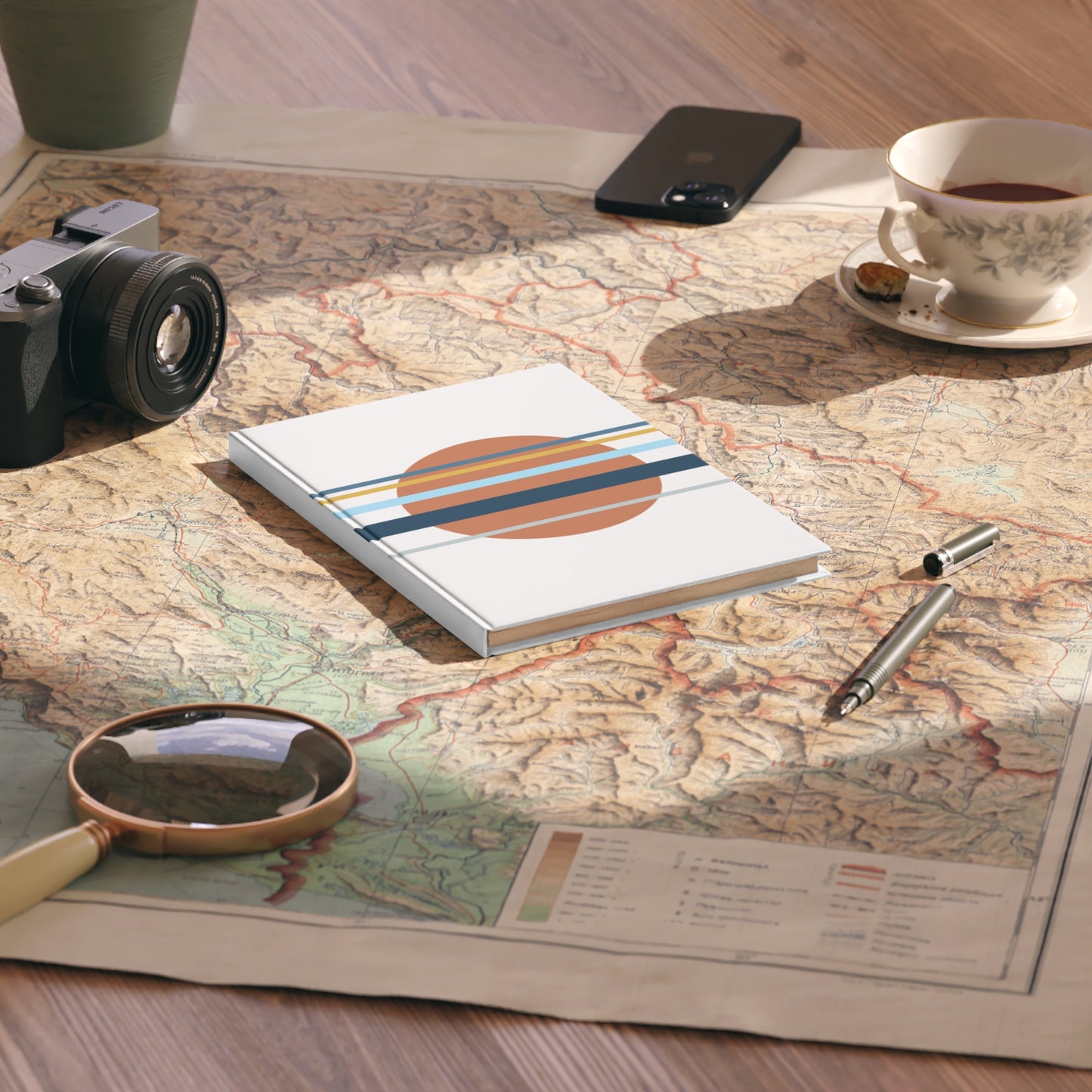 Notebook with travel-themed design on a map with camera, magnifying glass, and cup of tea.