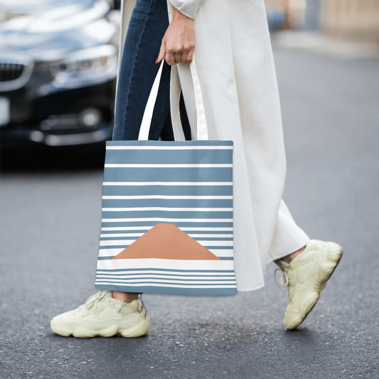 Person holding a blue and white striped tote bag with a mountain design on a street.