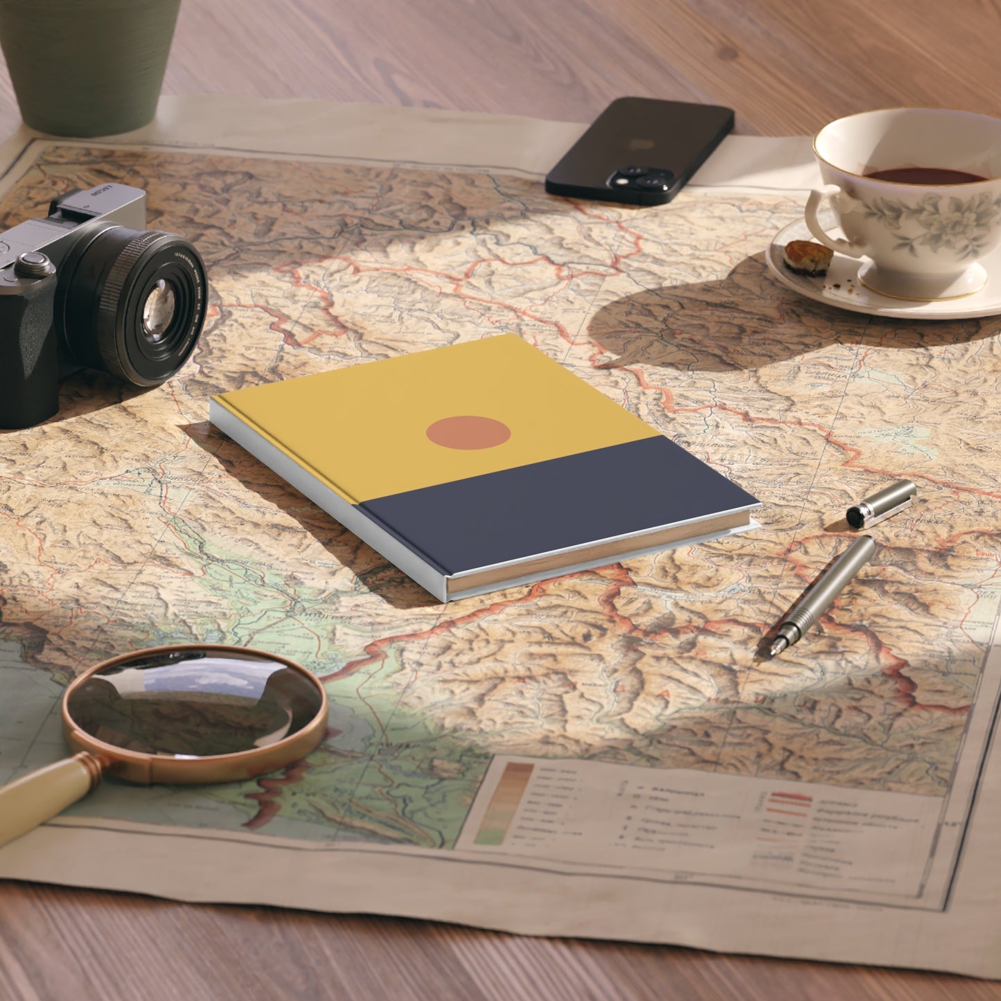 Notebook on a map with a camera, phone, cup, and pen nearby
