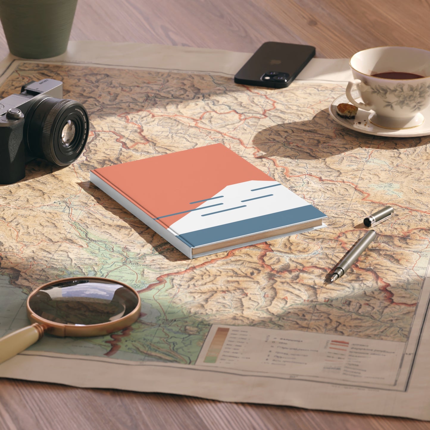 Notebook on a map with a camera, magnifying glass, and cup of tea.