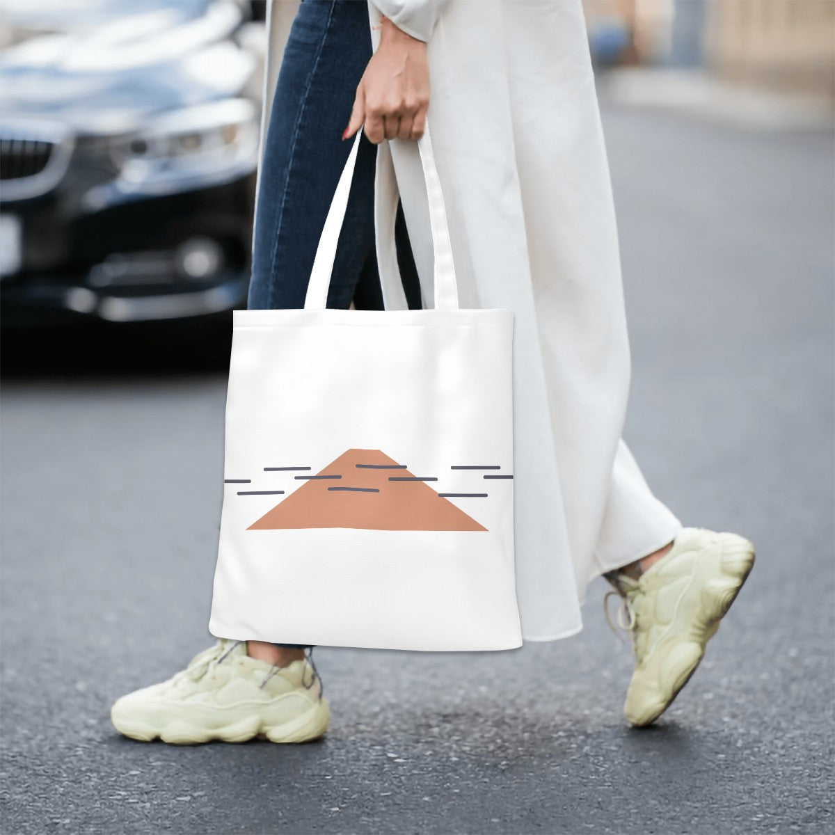 Person walking on a street holding a white tote bag with a geometric design.