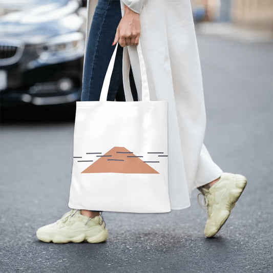 Person walking on a street holding a white tote bag with a geometric design.
