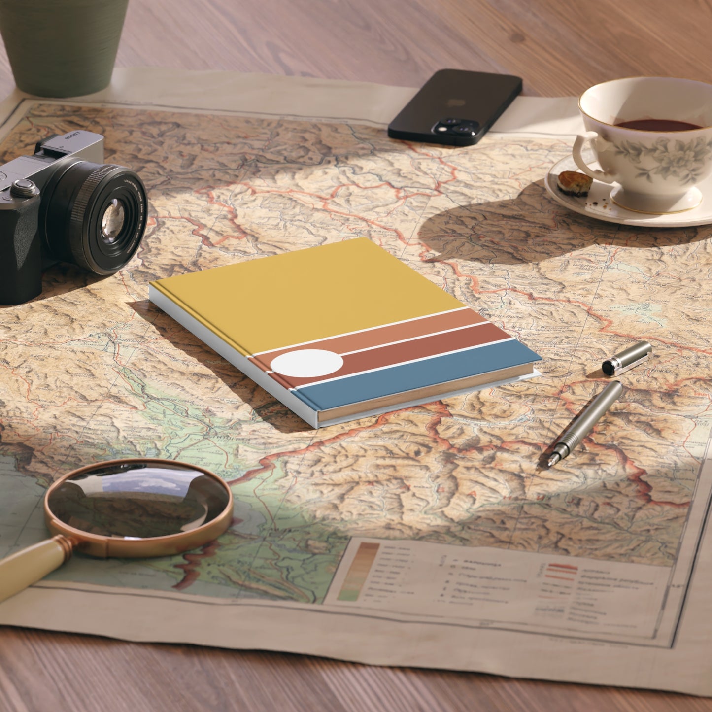 Notebook with colorful design on a map with camera, phone, cup, and pen.