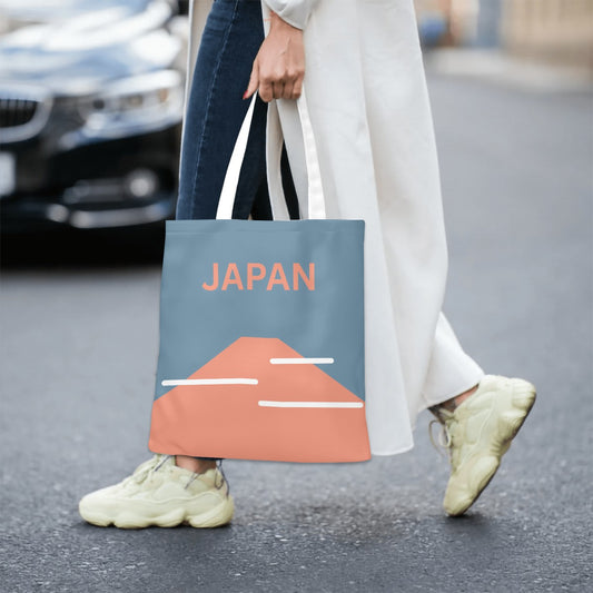 Person holding a tote bag with 'JAPAN' and mountain design on a street.