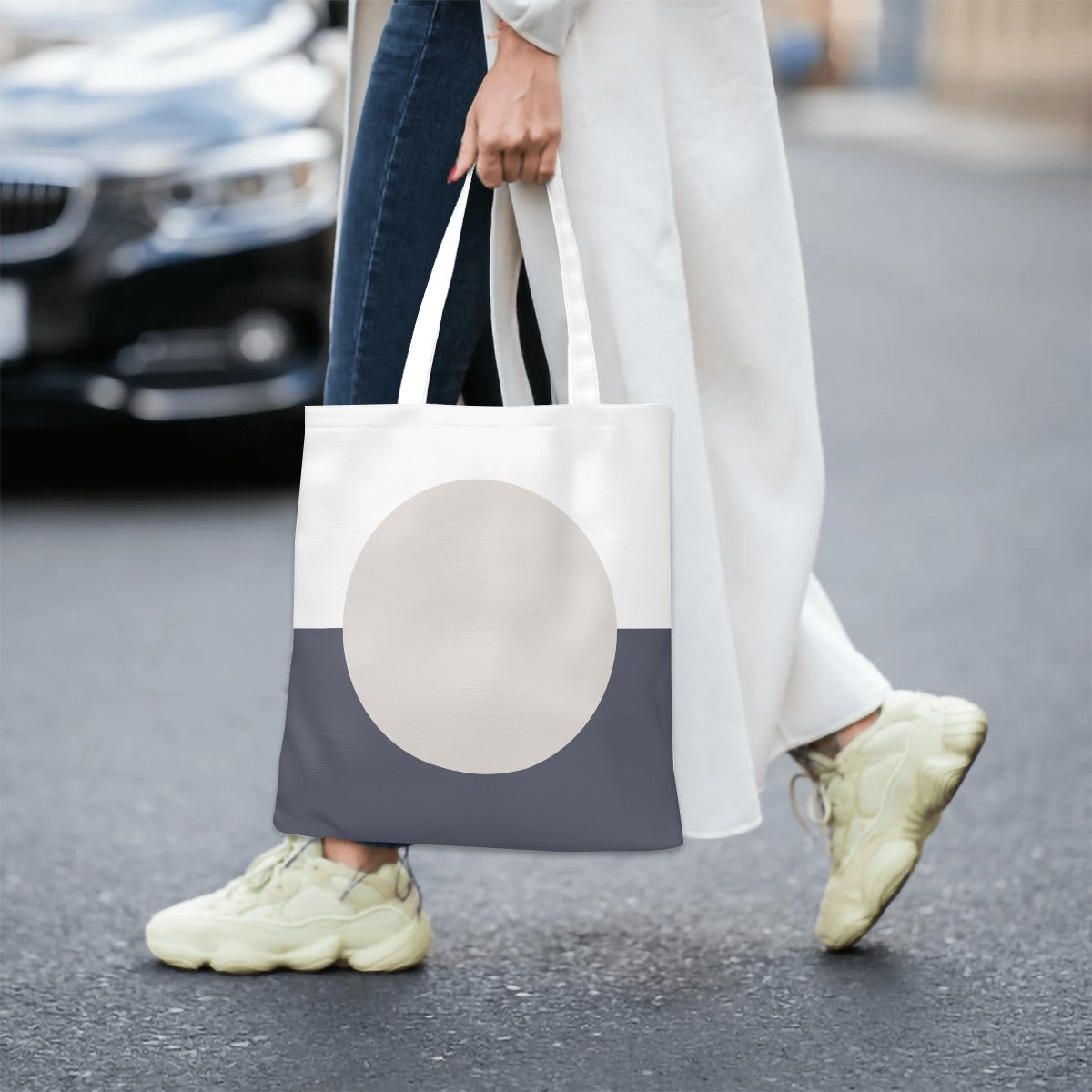 Person holding a tote bag with a large circle design on a street.