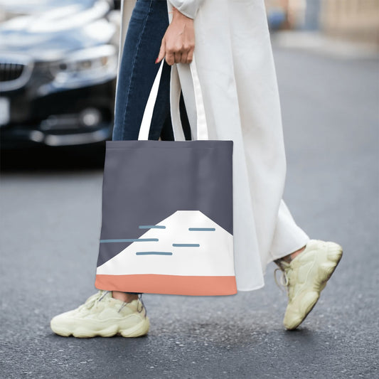 Person holding a tote bag with a mountain design on a street.