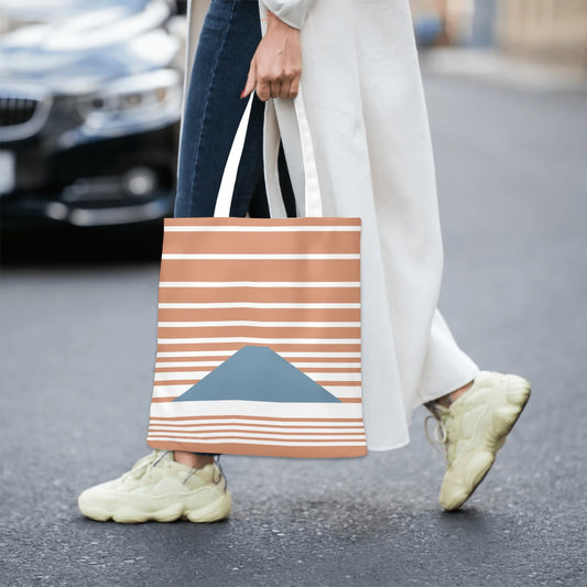 Person walking on a street holding a striped tote bag with geometric design.
