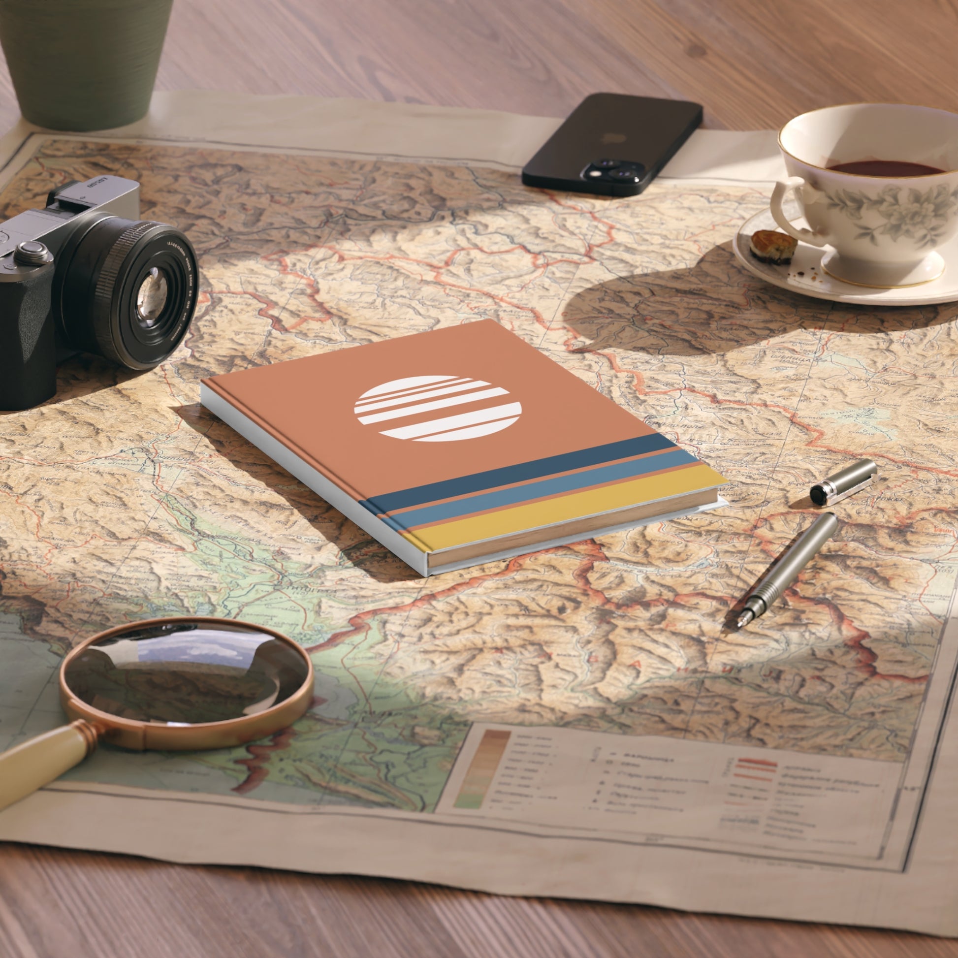 Notebook with a colorful design on a map with a camera, phone, and tea cup.