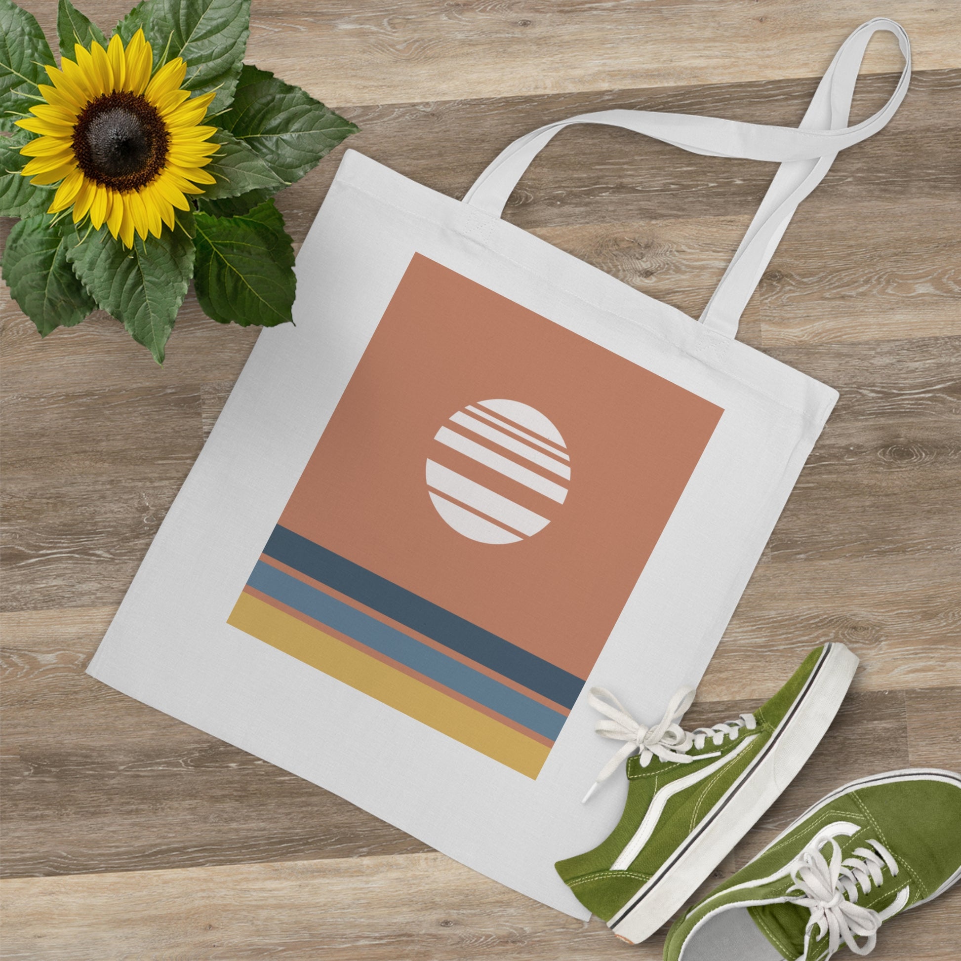 Tote bag with a sun design, green sneakers, and a sunflower on a wooden surface