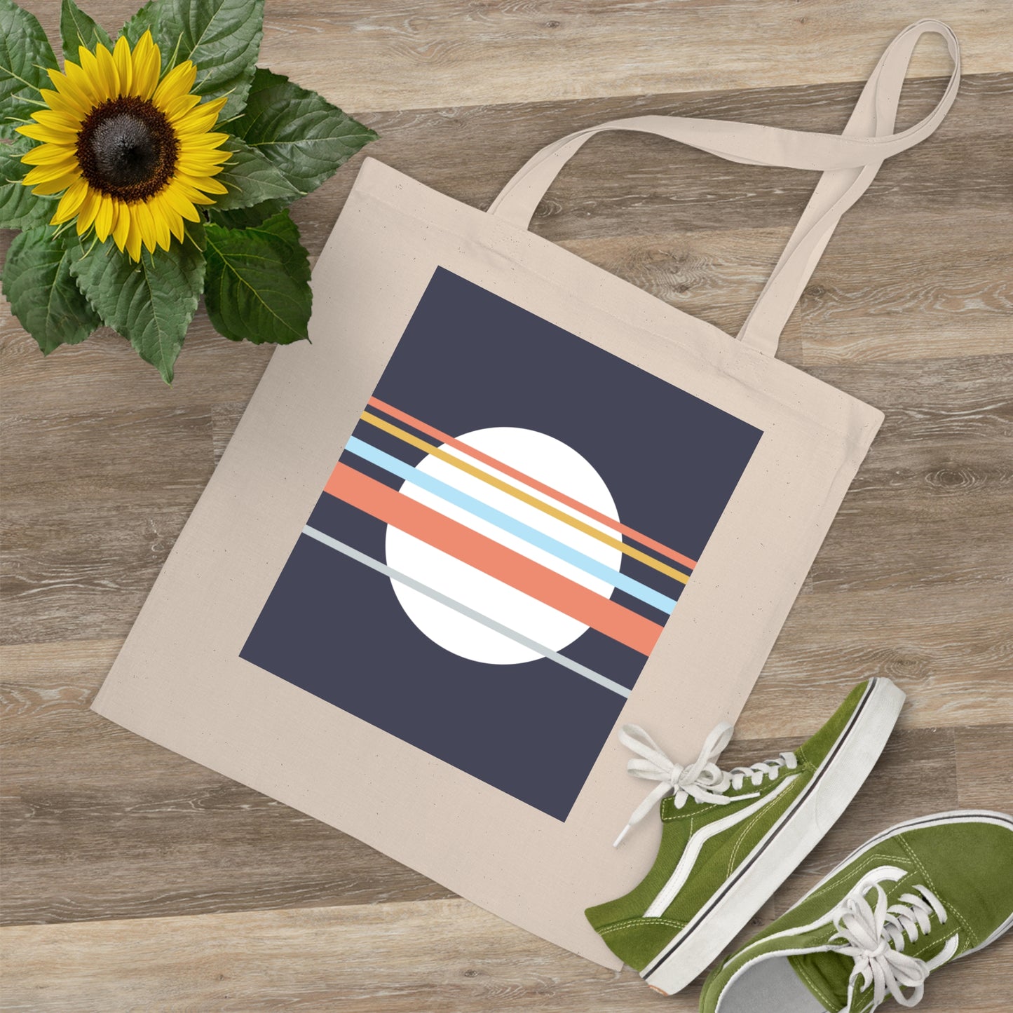Tote bag with a colorful design on a wooden surface with a sunflower and green shoes.