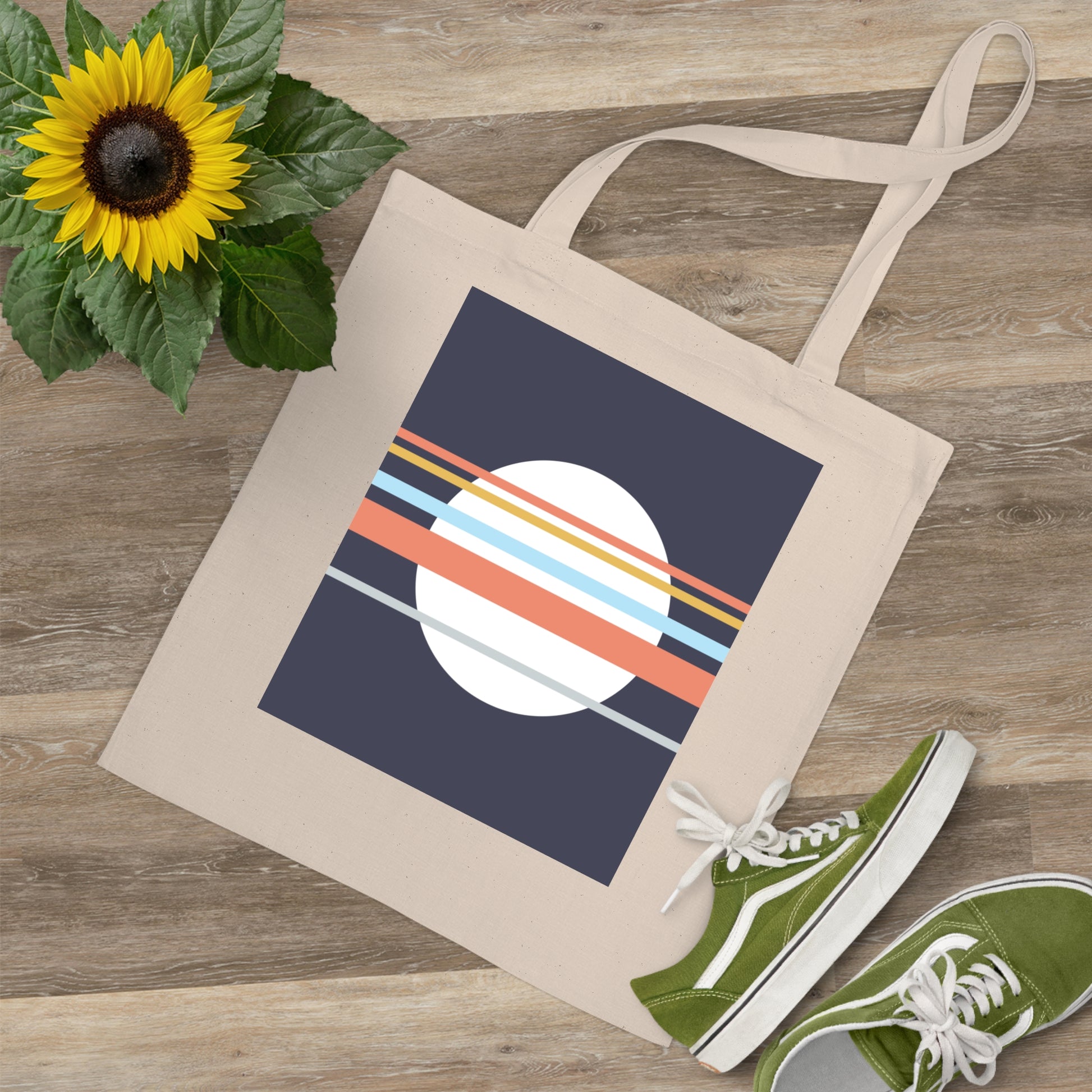 Tote bag with a colorful design on a wooden surface with a sunflower and green shoes.