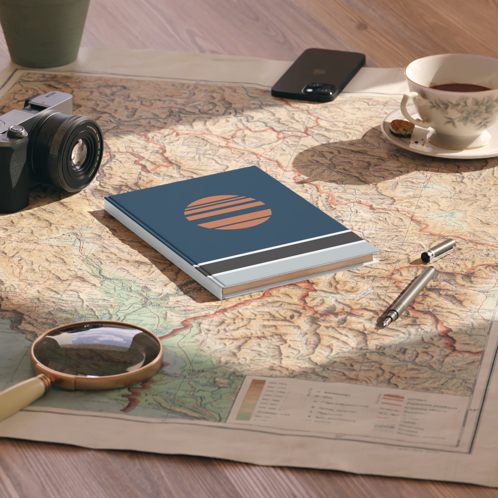 Notebook with a sun design on a map with a camera, phone, and tea cup.